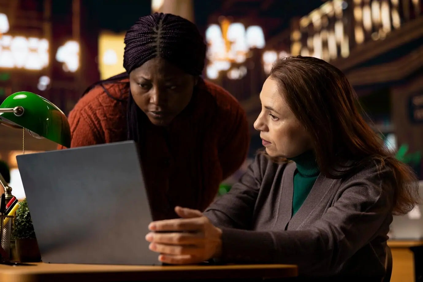 Взрослые студенты за столом в библиотеке изучают материалы на ноутбуке.